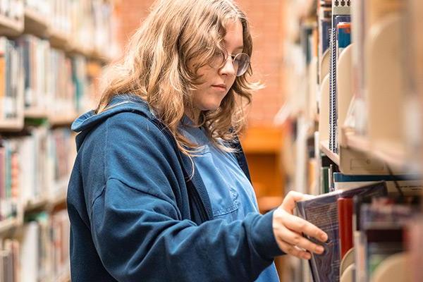 Student pulling book from library shelf