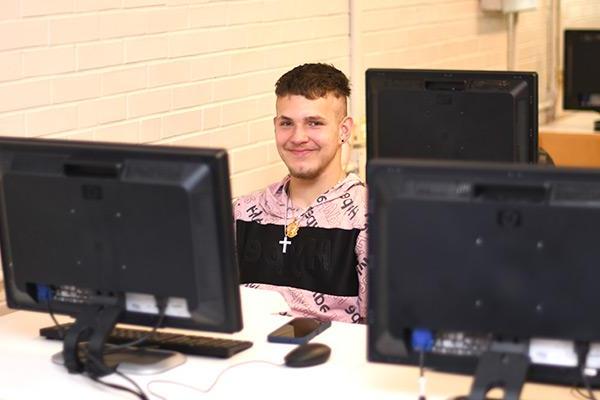 Student smiling, sitting between computers 